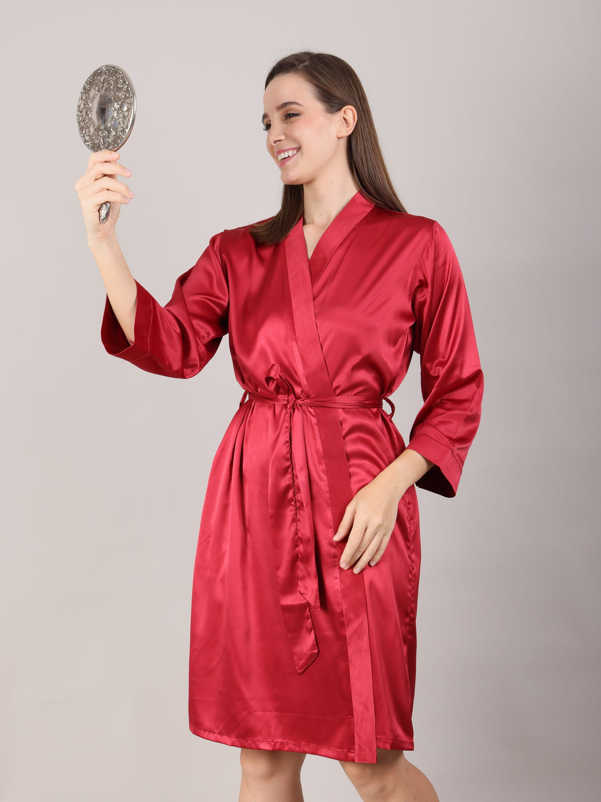 Woman wearing a red satin robe holding a mirror during her make up for marriage