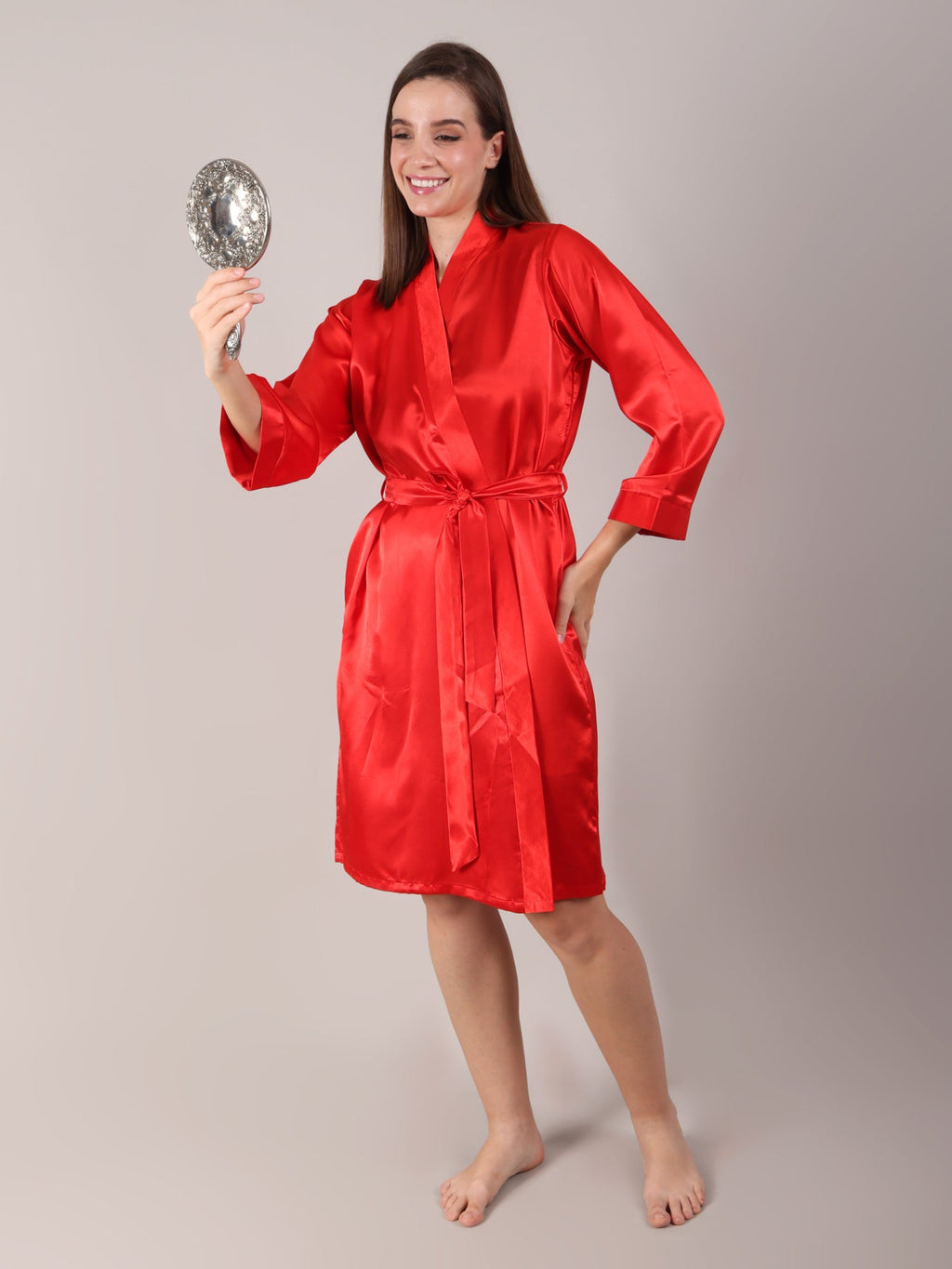 Woman wearing a red satin robe holding a silver mirror for getting ready moments and photo shoot for her marriage.