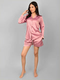 A woman standing in a rosette pink satin nightsuit with long sleeves, a shirt, and shorts, posing for the camera.