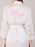 White satin robe with 'Bride' embroidered on the back, worn by a bride for her makeup shoot.